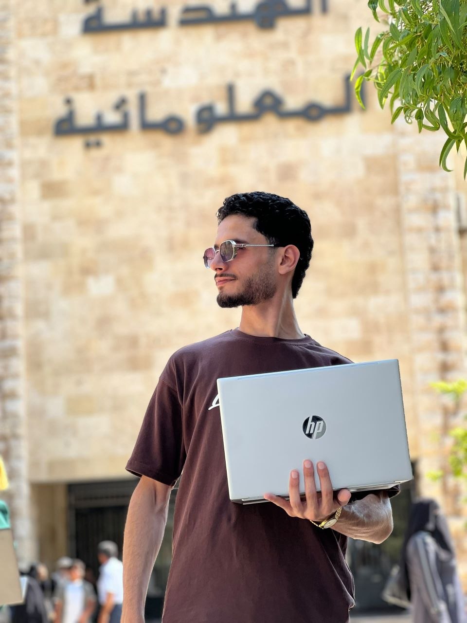 إبراهيم الحسين مطور تطبيقات يحمل حاسوبه أمام كلية الهندسة المعلوماتية